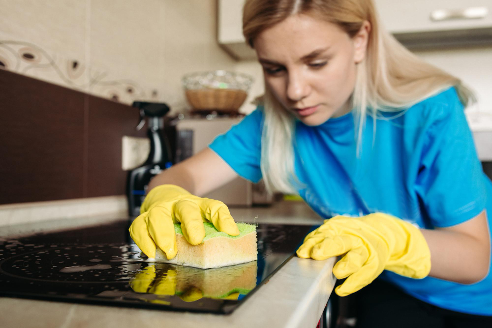 close-up-woman-wearing-protective-glove-with-rag-cleaning-electric-stove-home-kitchen-beautiful-girl-washing-black-shiny-surface-kitchen-top-hand-with-foam-sponge-housework-concept