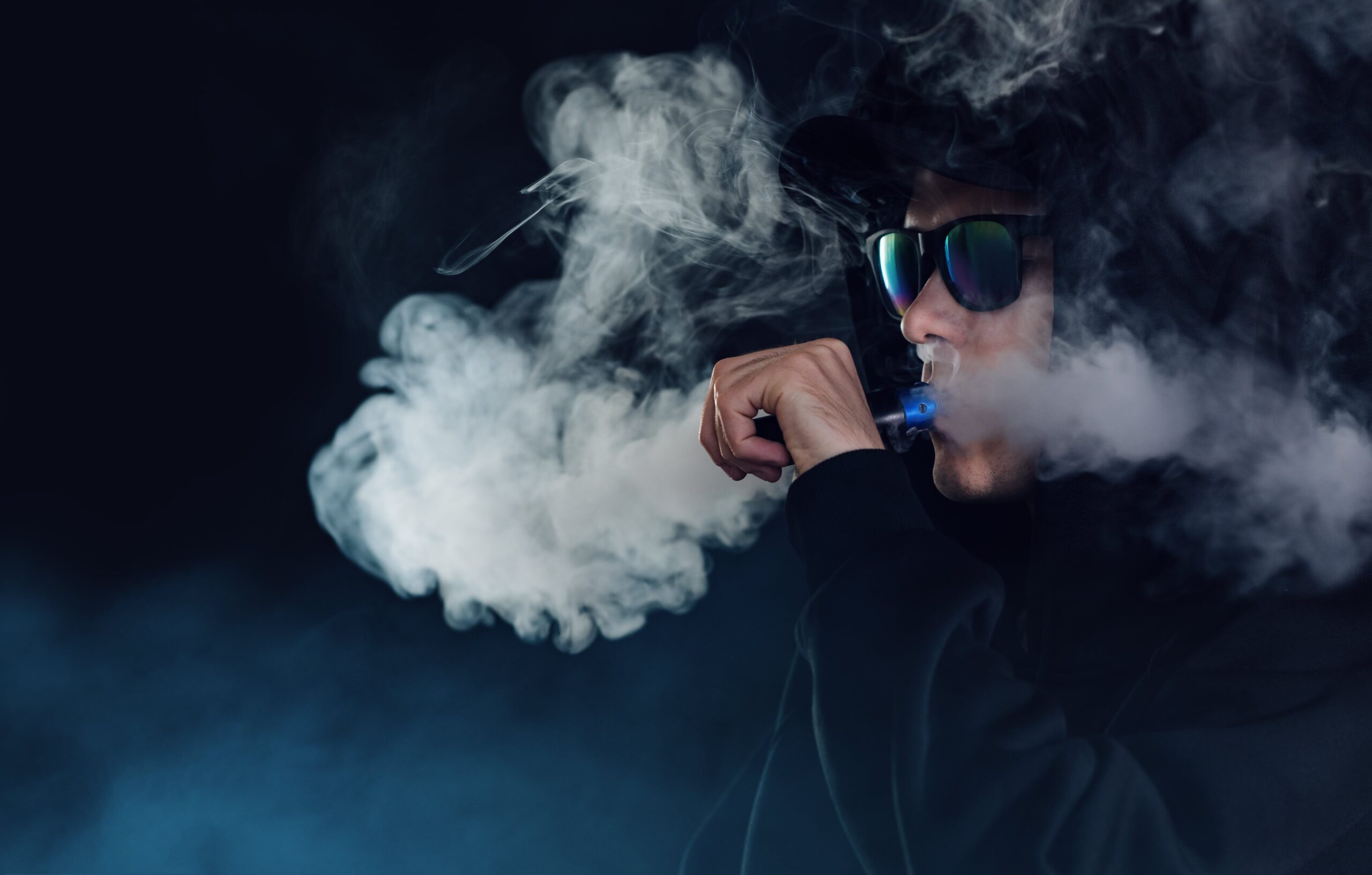 portrait-handsome-guy-black-hat-sunglasses-vaping-exhaling-cloud-vapor-from-e-cigarette-min