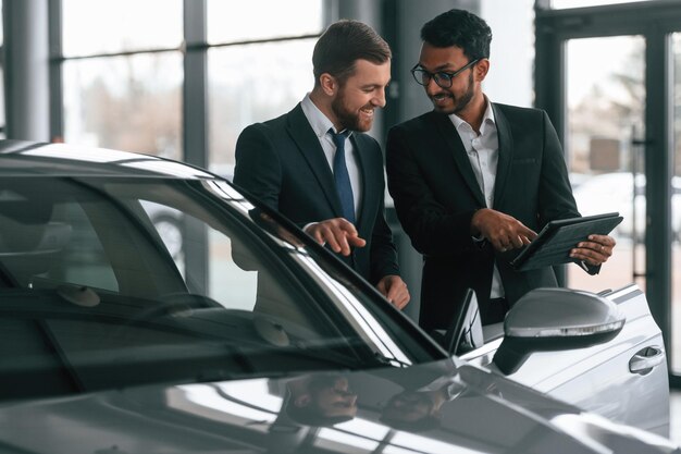 standing-near-automobile-with-graphic-tablet-two-businessmen-working-together-car-showroom_146671-89237