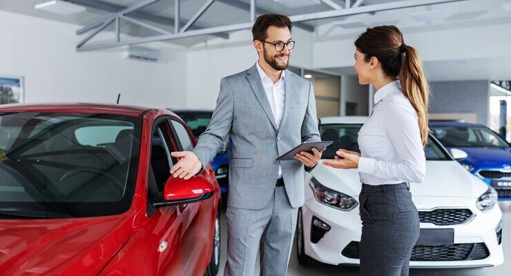 smiling-car-seller-standing-car-salon-with-customer-showing-around-cars-sale_232070-12340