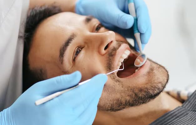 smiling-young-man-sitting-dentist-chair-while-doctor-examining-his-teeth_158595-7733